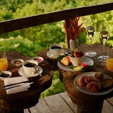 Jungle sunrise breakfast at Amanera with fresh fruit, pastries, and coffee laid out on a wooden table overlooking green vegetation.