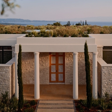 三间卧室别墅入口，安缦卓熠度假村，希腊，石墙和木门，远处可见爱琴海景观。