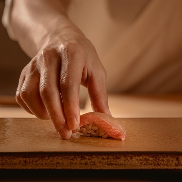 Hand reaching for sesame-crusted appetiser at Aman Nai Lert Bangkok dining venue.
