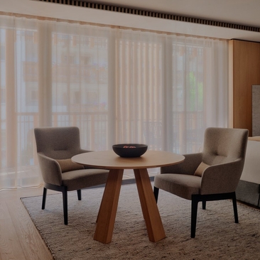 Deluxe room seating area at Aman Rosa Alpina with two chairs and wooden table by sheer curtained windows.
