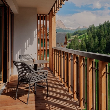Deluxe Suite balcony at Aman Rosa Alpina with woven chair overlooking Dolomite mountains and forested valley.