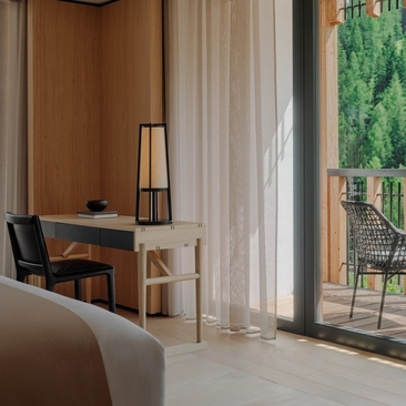 Deluxe Suite with forest views at Aman Rosa Alpina, featuring a workspace and floor-to-ceiling windows overlooking Italian woodland.