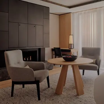 Premier Room at Aman Rosa Alpina resort, featuring a seating area with two upholstered chairs, wooden table and floor-to-ceiling wardrobe.