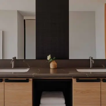 Bathroom at Aman Rosa Alpina resort featuring dual basins, dark accent wall, and wooden cabinetry.
