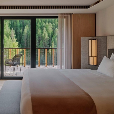 Premier Suite at Aman Rosa Alpina with dual beds and views of forested Italian Alps through floor-to-ceiling doors.
