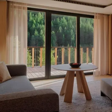 Premier Suite at Aman Rosa Alpina resort with seating area and view to alpine landscape through glass doors.