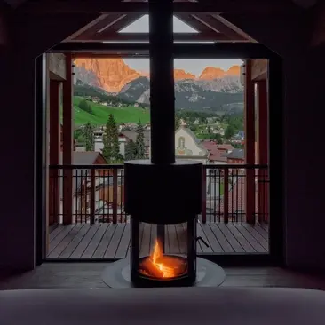 Porte aperte di una suite che affacciano su verdi valli alpine, con stufa a legna accesa ad Aman Rosa Alpina.