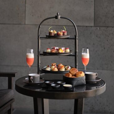 Afternoon tea service at Aman Tokyo with tiered stand, pastries, and champagne on black table.