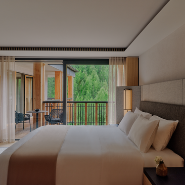 Aman Suite bedroom at Aman Rosa Alpina with bed facing open doors to mountain-view balcony.