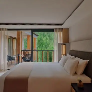 Aman Suite bedroom at Aman Rosa Alpina resort, with bed facing open doors to a mountain-view balcony.