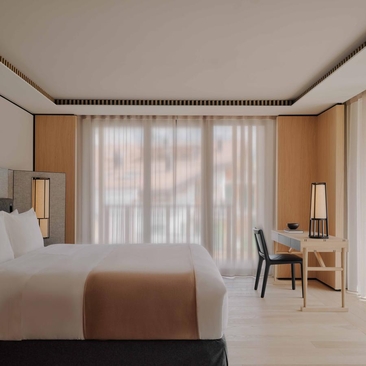 Deluxe Suite with village views at Aman Rosa Alpina, featuring a bed with brown throw, floor-to-ceiling windows and wooden furnishings.