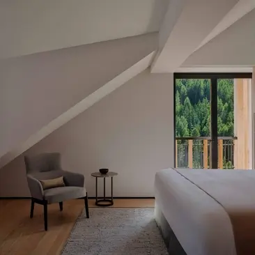 Dolomites Suite bedroom at Aman Rosa Alpina resort, with sloped ceiling, armchair and mountain views.