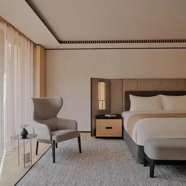 Rosa Alpina Suite bedroom with bed, grey armchair and floor-to-ceiling windows at Aman Rosa Alpina resort.