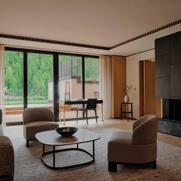 Rosa Alpina Suite with seating area, floor-to-ceiling windows overlooking Alpine landscape, at Aman Rosa Alpina resort.