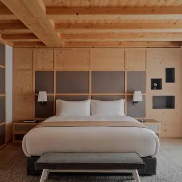 Zeno Suite principal bedroom with warm wood panelling and neutral bedding at Aman Rosa Alpina resort.