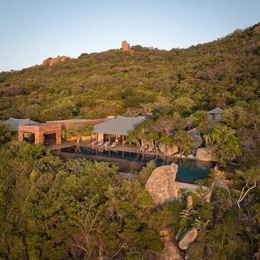 Aerial view of Amanoi's Ocean Pool Residence nestled into a verdant hillside in Vietnam, with terracotta-roofed structures and a curved pool.
