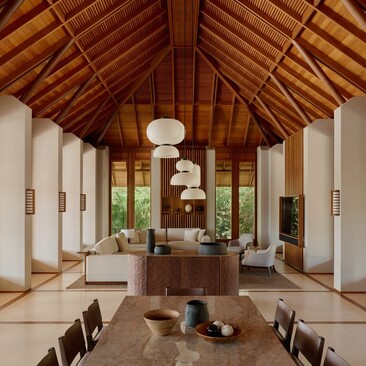 Amanyara villa living area with wooden pitched ceiling, white walls, and central stone fireplace, viewed from entrance.