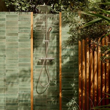 Outdoor shower at Amanyara with green tile walls and wooden screen, dappled with foliage shadows.