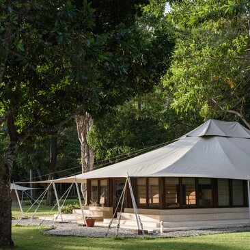 Jungle tent accommodation at Amanwana with candlelit exterior seating amongst trees at dusk.