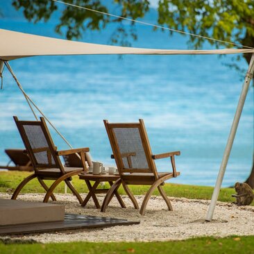 Two wooden deck chairs facing the ocean at Amanwana, Indonesia, beneath a canvas canopy.