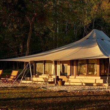 Canvas tent illuminated at dusk at Amanwana, Indonesia, with ocean view and surrounding trees.
