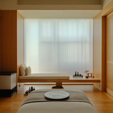 Single treatment room at Aman Tokyo with meditation cushion facing sheer-curtained window and wooden shelf.