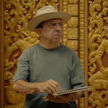 Paul Bloxham sketches at Amantaka, Laos, with ornate golden temple panels in the background.