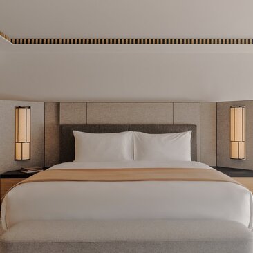 Serene hotel bedroom at Aman Rosa Alpina with neutral tones, upholstered headboard and soft bedside lighting.
