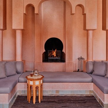 Villa with two bedrooms at Amanjena resort in Morocco, featuring a fireplace alcove and seating area with terracotta walls.