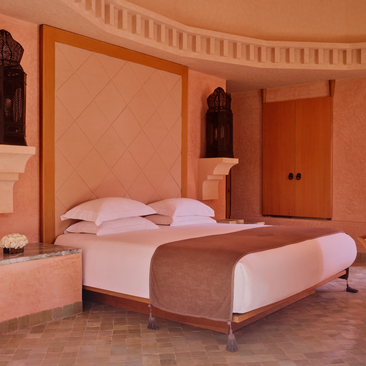 Principal bedroom at Amanjena resort with twin beds, terracotta walls, and Moroccan architectural details.