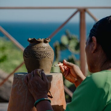 Artisan demonstrating traditional Cham pottery techniques at Amanoi, with coastal views beyond.
