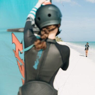 Kitesurfer in wetsuit holding kite at Amanpulo resort, Philippines, with beach and water visible behind.