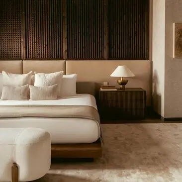 Serene bedroom in Aman New York with neutral linens, wood-paneled headboard, and soft lighting.