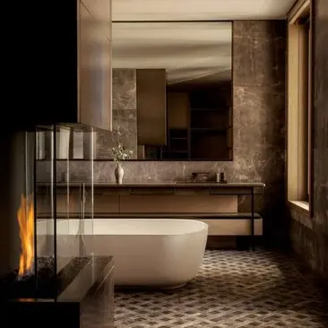 Bathroom in a three-bedroom penthouse at Aman New York, featuring a freestanding sofa-tub, illuminated mirror, and geometric floor tiles.