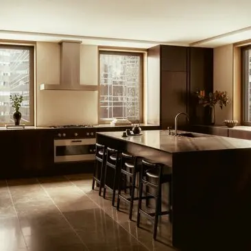 Kitchen area in a three-bedroom penthouse at Aman New York, featuring dark cabinetry, a central island, and floor-to-ceiling windows.