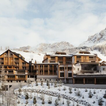 Aman Rosa Alpina exterior in winter, with snow-covered Dolomite peaks rising behind the wooden chalet-style hotel.
