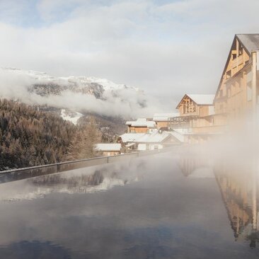 Aman Rosa Alpina's spa swimming pool reflects snow-capped mountains on a misty winter morning in Italy.