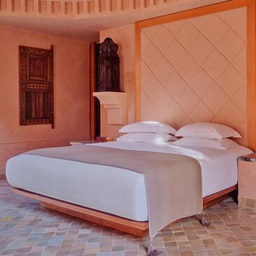 Pavilion bedroom at Amanjena resort with terracotta walls and wooden bed frame.