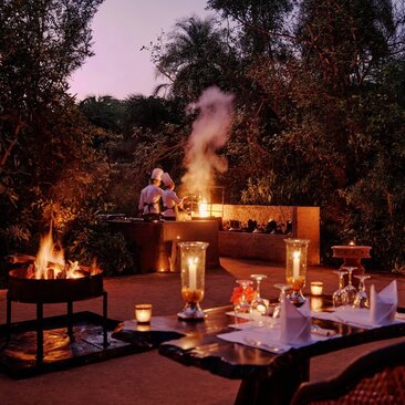 Candlelit outdoor dining setup at Amanbagh at dusk, with fire bowls illuminating the table amongst trees.