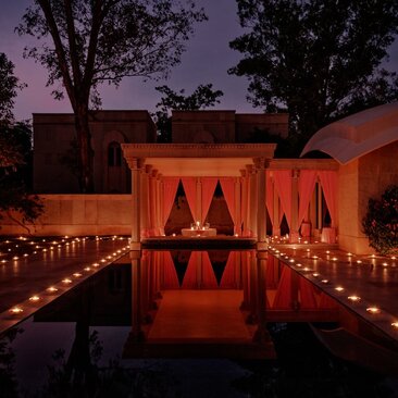 Candlelit private pool pavilion at Amanbagh at dusk, glowing with warm orange lighting.
