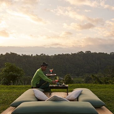 Sundowner cocktail served on a lounger overlooking verdant valleys at Amandari resort, Indonesia.