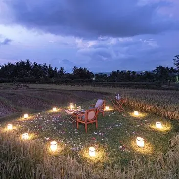 Sunset martini service set amongst rice fields at Amanjiwo, with candlelit tables glowing as dusk falls.