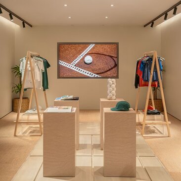 Aman Essentials pop-up shop at Amanpuri resort, displaying tennis wear and equipment on wooden stands beneath framed artwork.