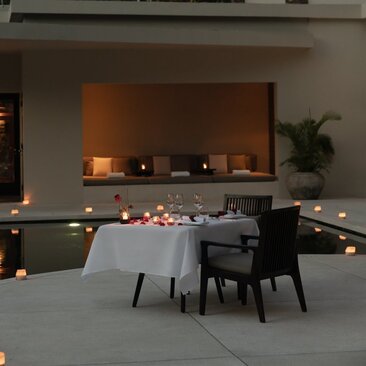 Candlelit dining table at Amansara with fireplace and soft amber lighting in the background.