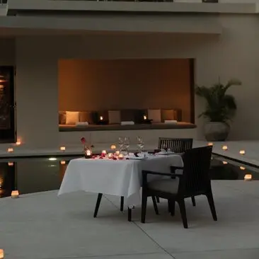 Candlelit dining table at Amansara with fireplace and soft amber lighting in the background.
