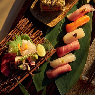 Sushi rolls and sashimi arranged on a green leaf plate at Aman New York's dining venue.