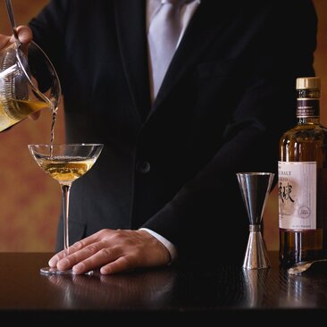 Bartender at Aman Venice pouring a cocktail, with bottles and glassware on the bar.
