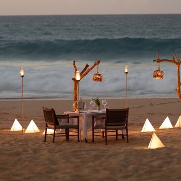 Cena privada en la playa al atardecer en Amanera, con mesas iluminadas frente al mar.