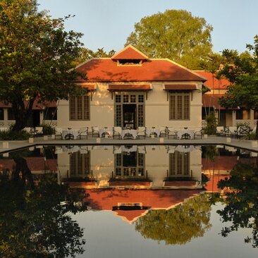 Amantaka's dining pavilion reflected in still water, framed by verdant trees.