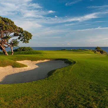 Trou 17 du parcours de golf Playa Grande à Amanera, avec bunker de sable et étang face à l'océan.